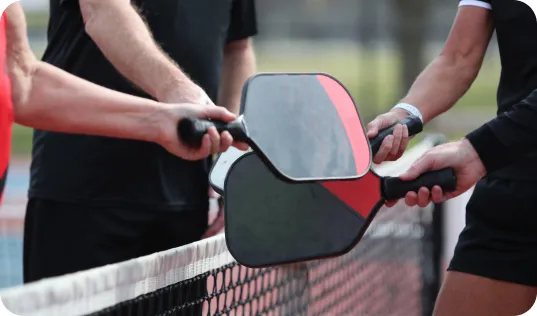 Pickleball players extending paddles together in a gesture of sportsmanship