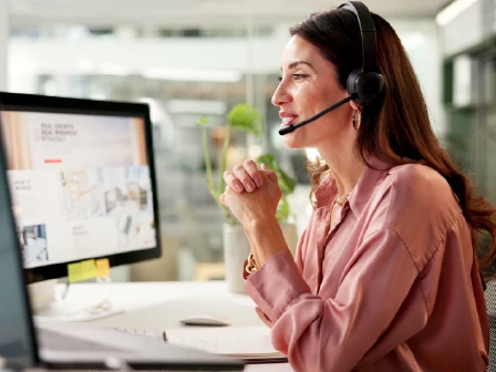 Woman talking into headset in front of computer screens with graphs